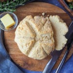 Damper 15 Close up cut damper on a chopping board with butter, bread knife and dishes on the sides, beetroot salad, mini roasted potatoes and slow cooker lam shoulder.