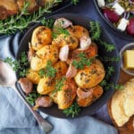 Roasted mini potatoes 14 Roasted mini potatoes in a serving dish garnished with fresh herbs, silver serving spoon to the side, fresh damper, pat of butter, beetroot salad and slow cooker roast lamb on the side.