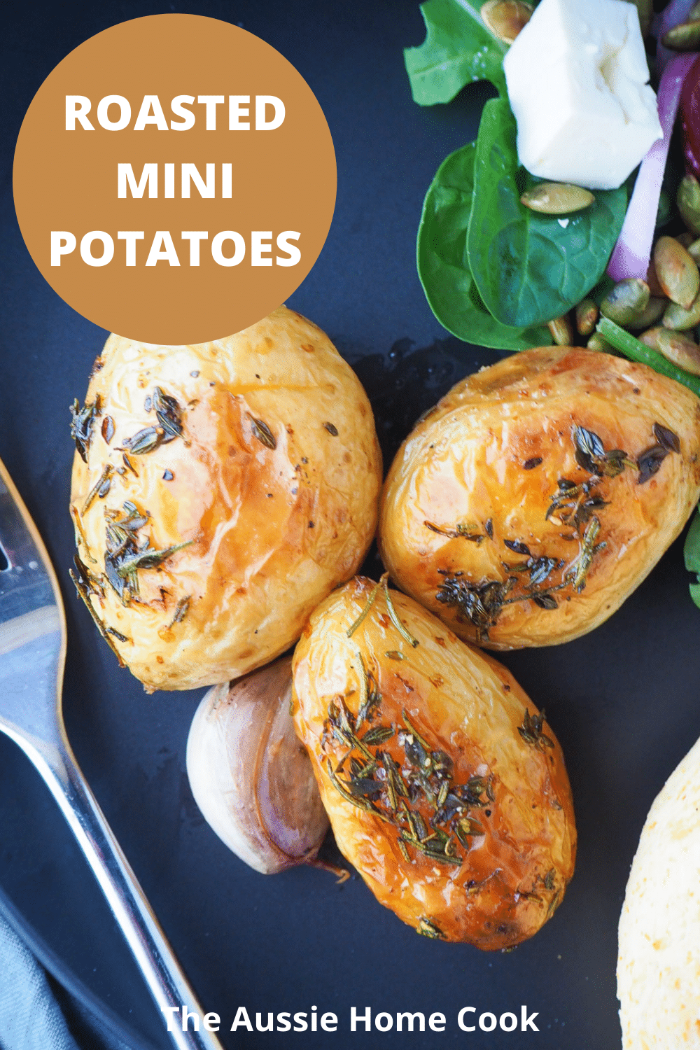 Roasted mini potatoes 15 Close up of roasted mini potatoes on a black plate, with beetroot salad on the side, silver fork and text overlay, roasted mini potatoes, The Aussie Home Cook.
