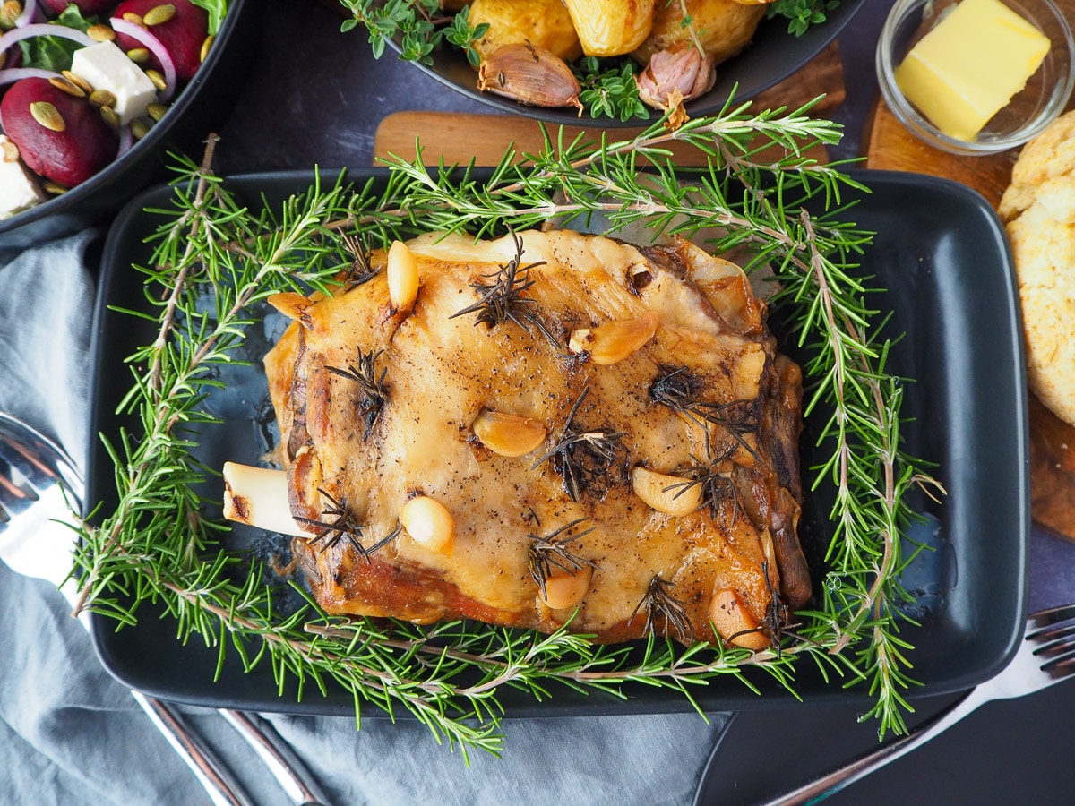 Slow cooker lamb shoulder 1 Slow cooker lamb roast on a serving plate, garnished with fresh rosemary, with damper, beetroot salad and roasted mini potatoes on the side.