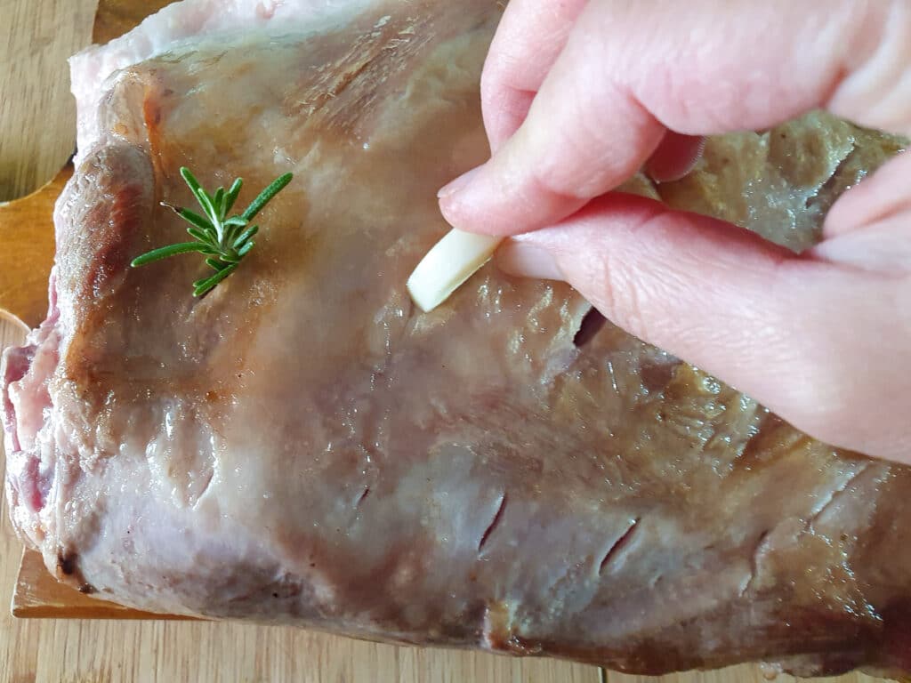 Slow cooker lamb shoulder 9 Inserting garlic sprigs into cut slits in roast.