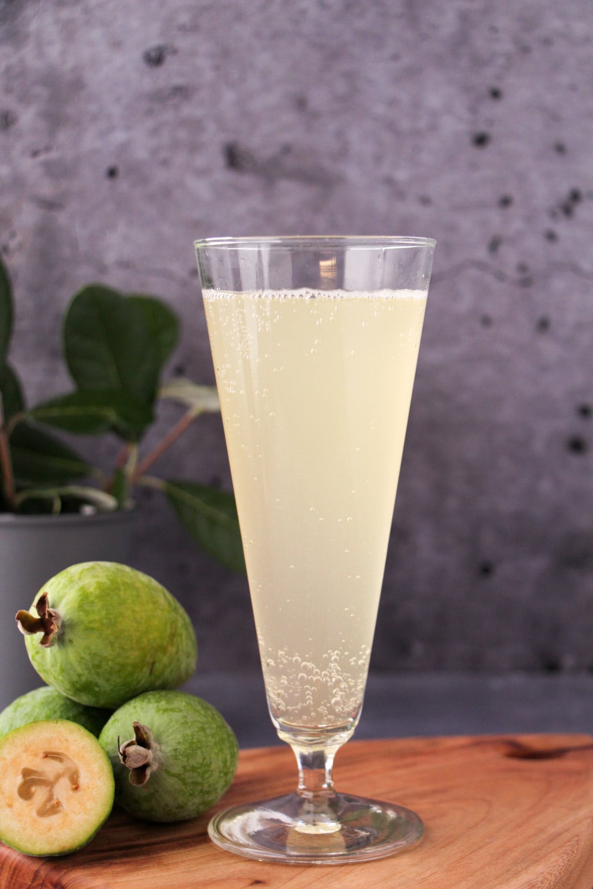 Feijoa fizz 15 Tall glass of feijoa fizz on a board, with fresh feijoas and feijoa leaves.
