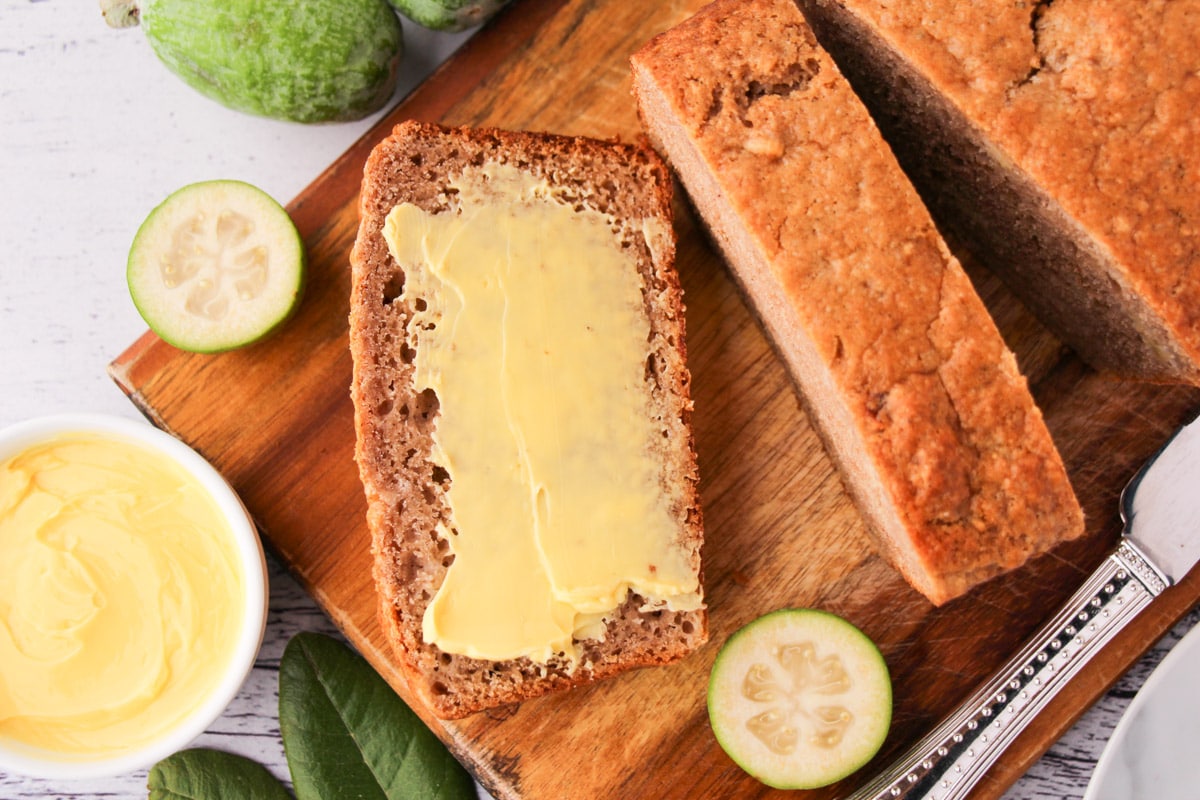 Feijoa loaf 1 Sliced feijoa loaf on a chopping board, with one buttered slice, fresh feijoas and leaves and a butter knife.
