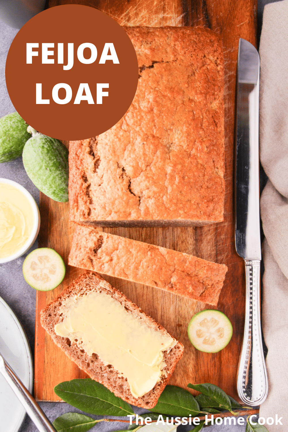 Feijoa loaf 19 Sliced feijoa loaf on a chopping board, with one buttered slice, fresh feijoas and leaves, large cutting knife, butter and plate and knife on the side, with text overlay, feijoa loaf and The Aussie Home Cook.