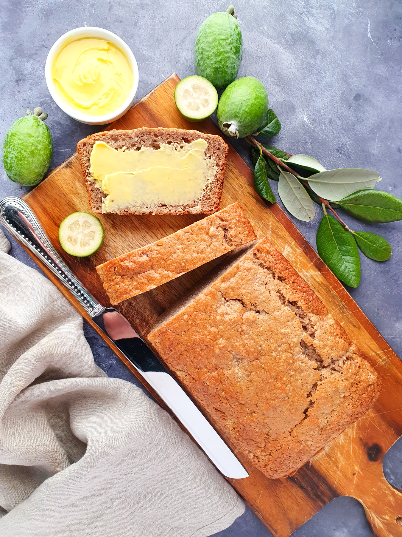 Feijoa loaf 20 Sliced feijoa loaf on a chopping board, with one buttered slice, fresh feijoas and leaves and a butter knife.