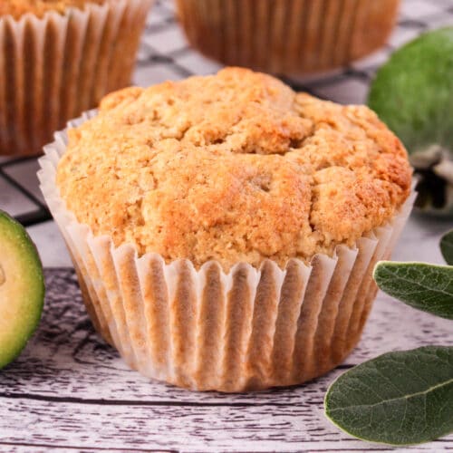 Feijoa muffins 6 Close up feijoa muffins with fresh feijoas and feijoa leaves, with extra muffins on a cooling rack in the background.