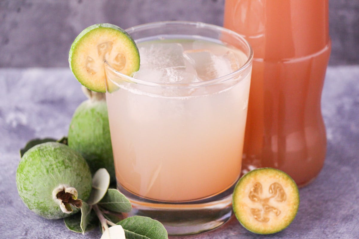 Feijoa syrup 11 Glass of made up feijoa syrup with ice and fresh feijoa garnish, with bottle of feijoa syrup and fresh feijoas and leaves.