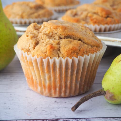Pear muffins 9 Close up pear muffin with fresh pears and tray of muffins in the background.