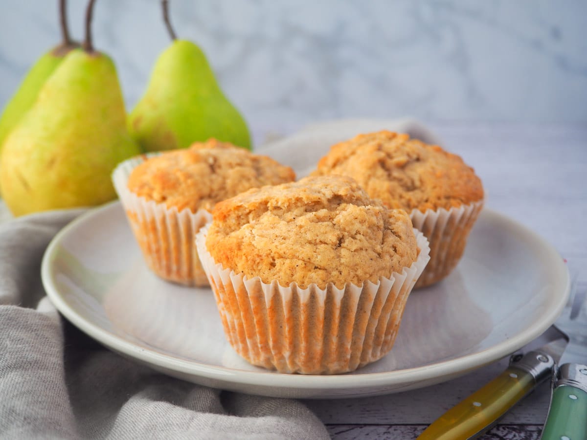 Pear muffins 14 Plate of three pear muffins, with forks and fresh pears in the background.