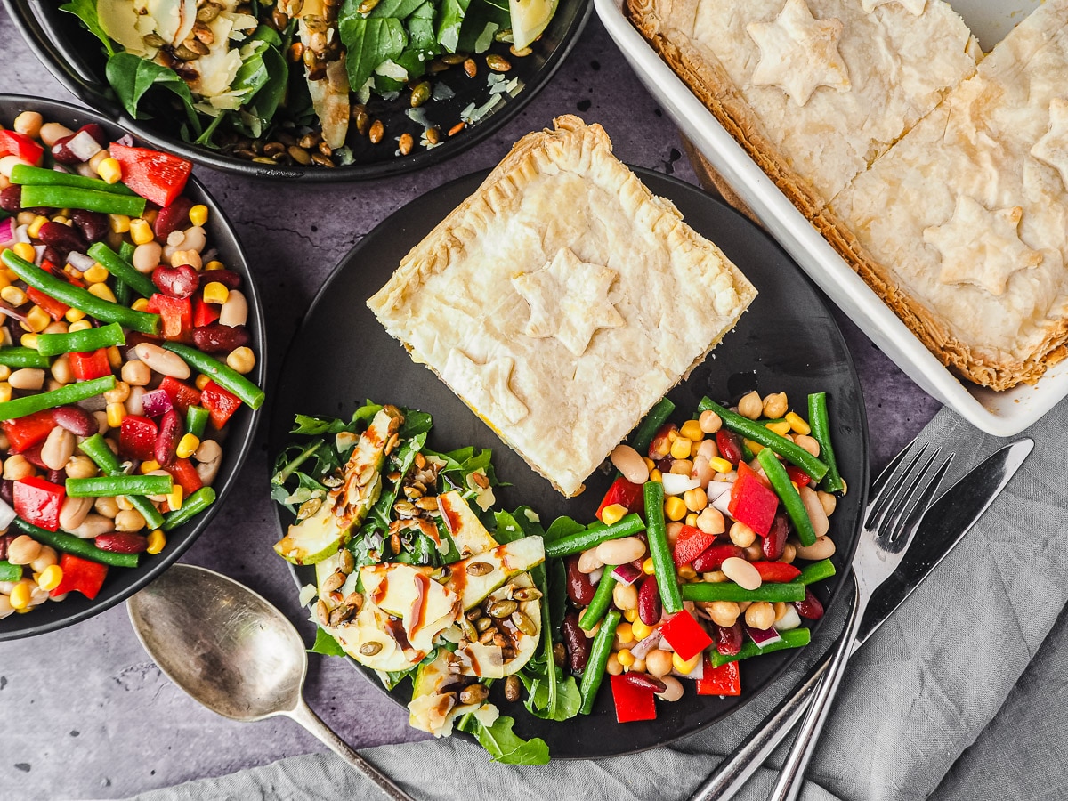Bacon and Egg Pie 2 Pie in a plate with salads, with pie dish and salads in background.