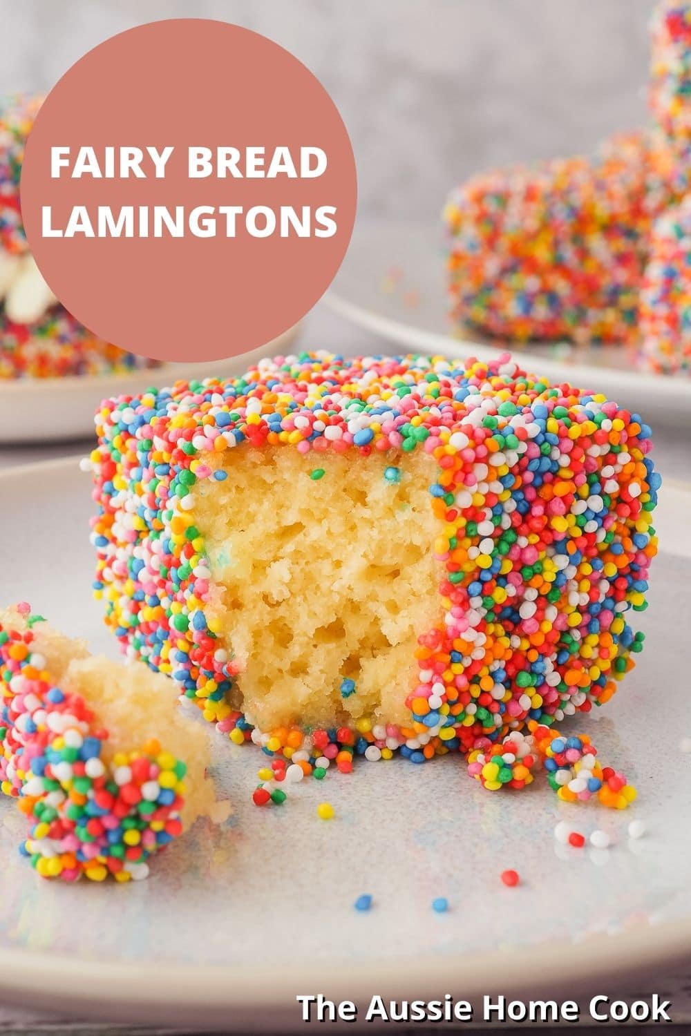 Fairy Bread Lamingtons 12 Lamington on a plate with one piece out, with lamingtons in the background and text overlay, Fairy Bread Lamingtons and The Aussie Home Cook.