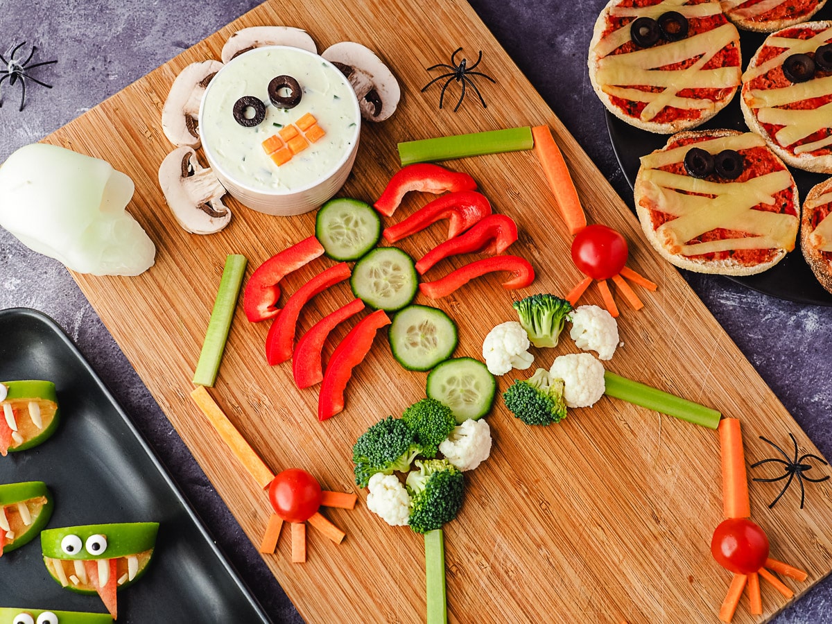 Skeleton Veggie Tray 2 Veggie tray on a board, with halloween skull and spiders, surrounded by Halloween party food, apple monsters and mummy pizzas.