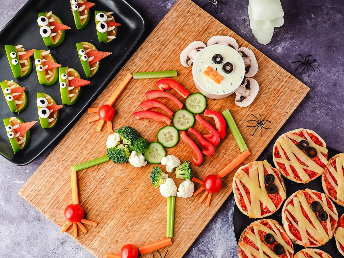 Skeleton Veggie Tray 6 Veggie tray on a board, with halloween skull and spiders, surrounded by Halloween party food, apple monsters and mummy pizzas.