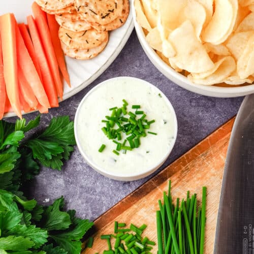 Sour Cream Dip 22 Sour cream dip garnished with fresh chives, with a bowl of chips, plate of crackers and carrot sticks, and chopping board with freshly chopped chives.
