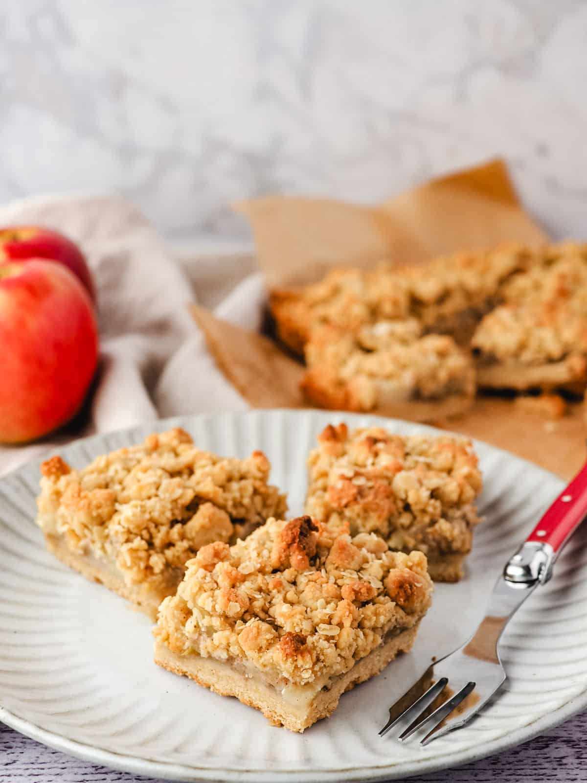 Apple Slice 12 Three pieces of apple slice on a plate with a fork and rest of slice in the background.