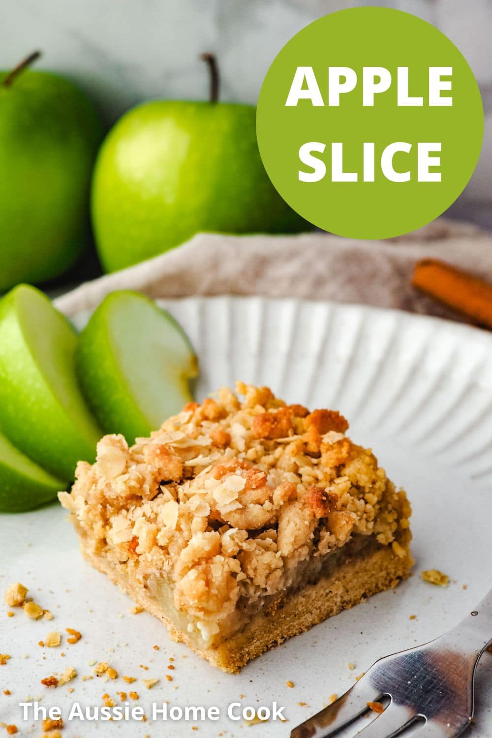 Apple Slice 11 Piece of apple slice on a plate with a fork and fresh apple on the side and fresh apples in the background.